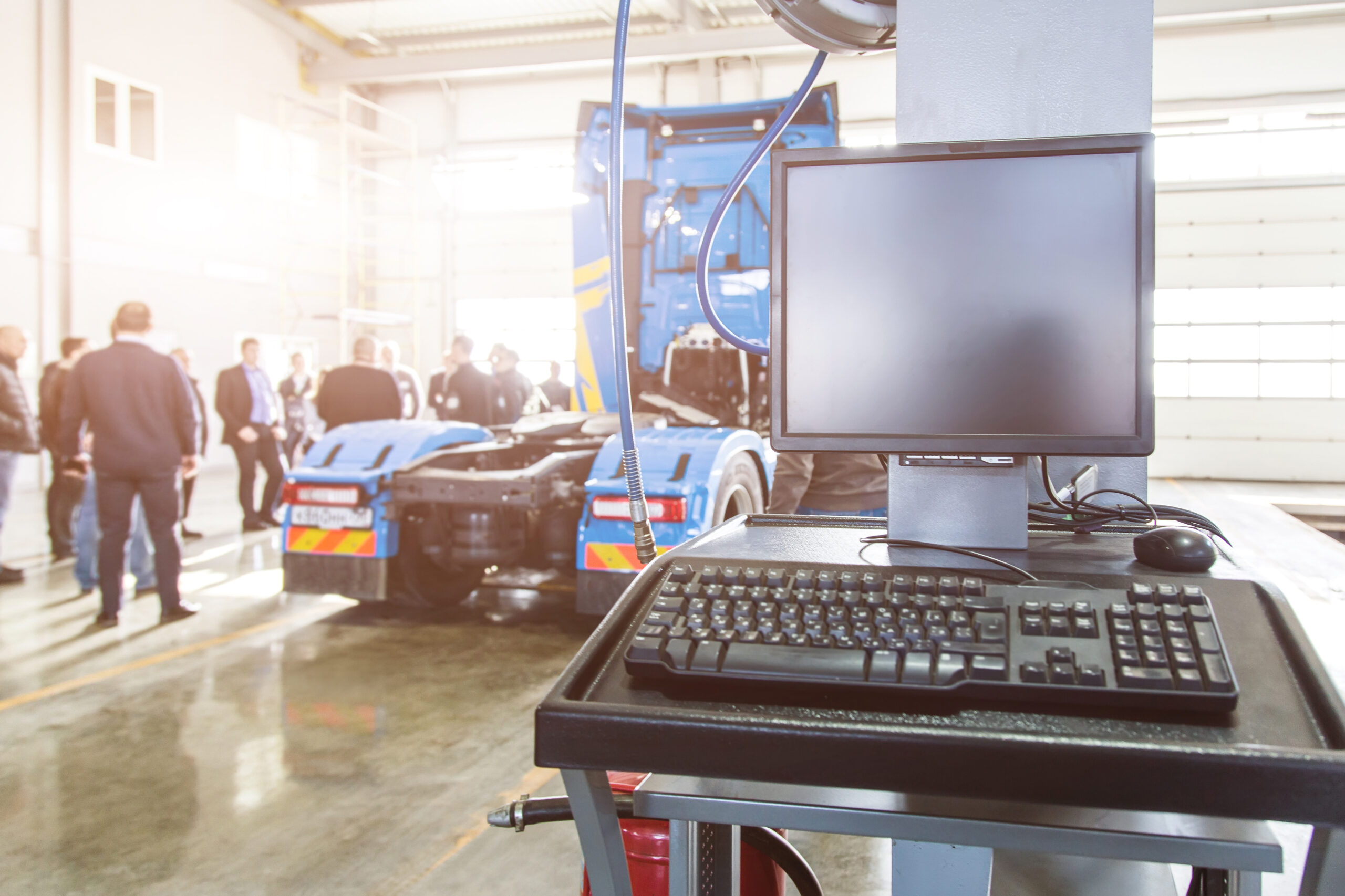 Monitor and keyboard at a stationary service point of trucks in a large garage and people in the background. Professional computer diagnostics of technical condition and malfunctions. Checking engine