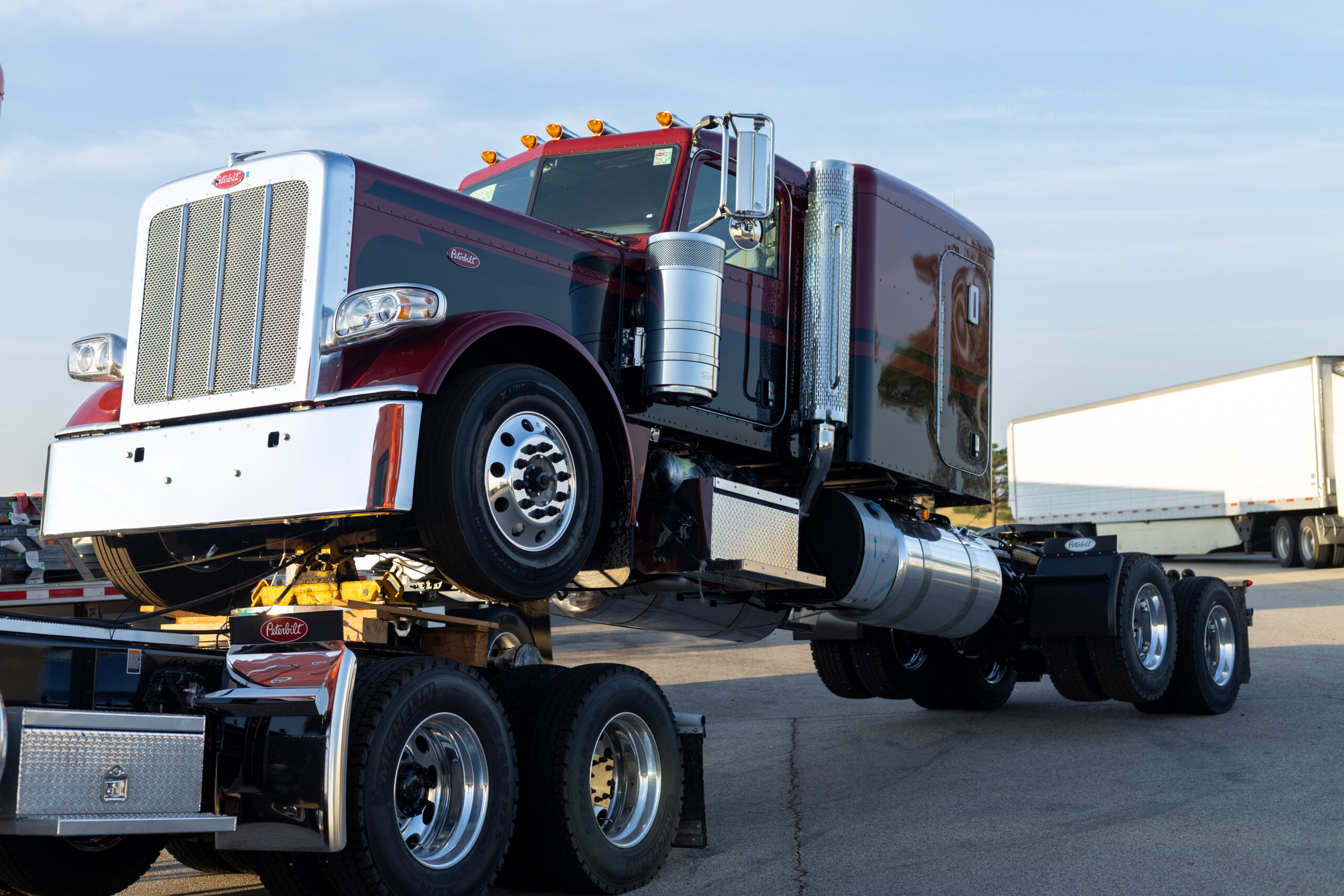 Port Arthur, Texas, USA - 09.11.2023: Semi Trucks Parked in a Row at Truck Stop During Dusk. Red Semi Truck Towed on a Trailer at Truck Stop